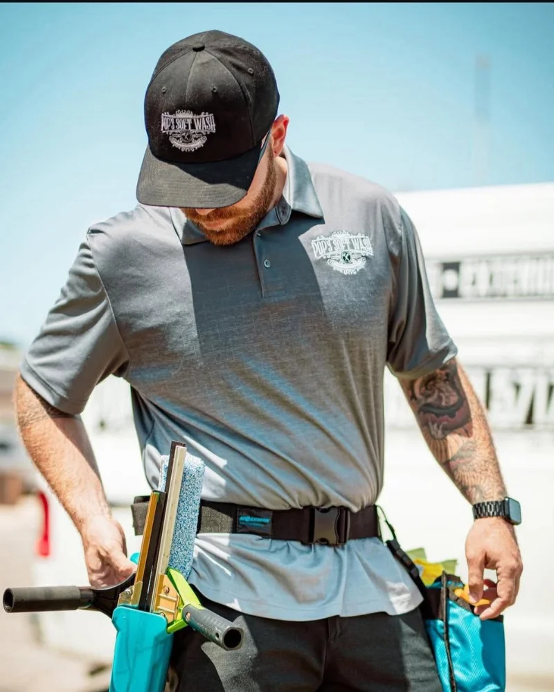 An exterior cleaning specialist wearing Pop's Soft Wash branded gear and adjusting a squeegee belt.